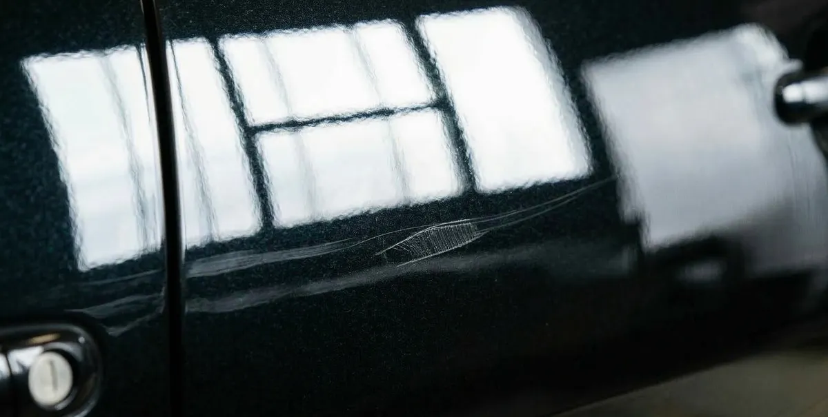 Krupni plan duboke ogrebotine koja je probila bezbojni lak na crnom automobilu
