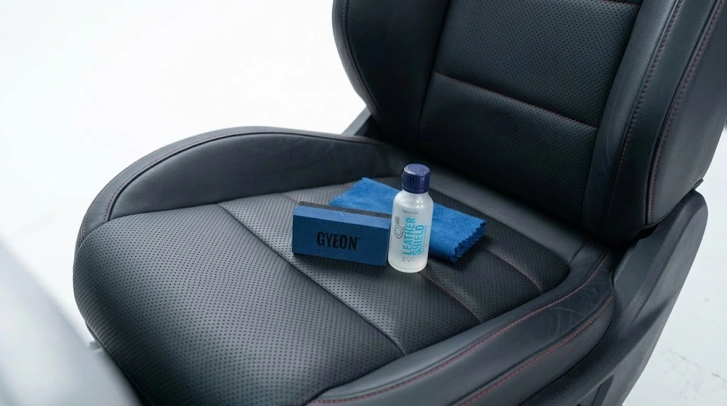 Gyeon LeatherShield EVO bočica, aplikator i mikrofiber krpa na crnom perforiranom kožnom sedištu pre tretmana zaštite