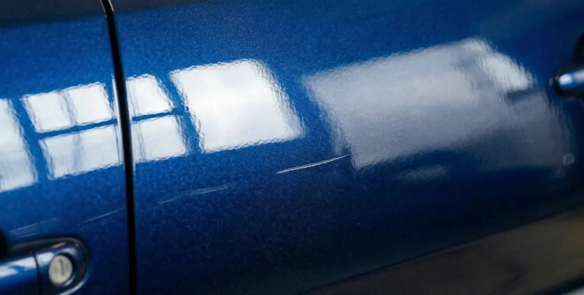 Duboka ogrebotina koja je probila bezbojni lak na plavom automobilu — primer trajnog oštećenja